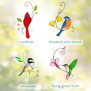Stained glass bird suncatchers collection featuring a red cardinal, bluebird with yellow leaves, chickadee, and green hummingbird with pink flower on decorative metal branches against a soft blurred background.