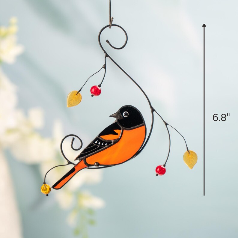 Close-up of a hanging stained glass oriole with yellow and red accents, next to a vertical measurement line showing 6.8 inches.