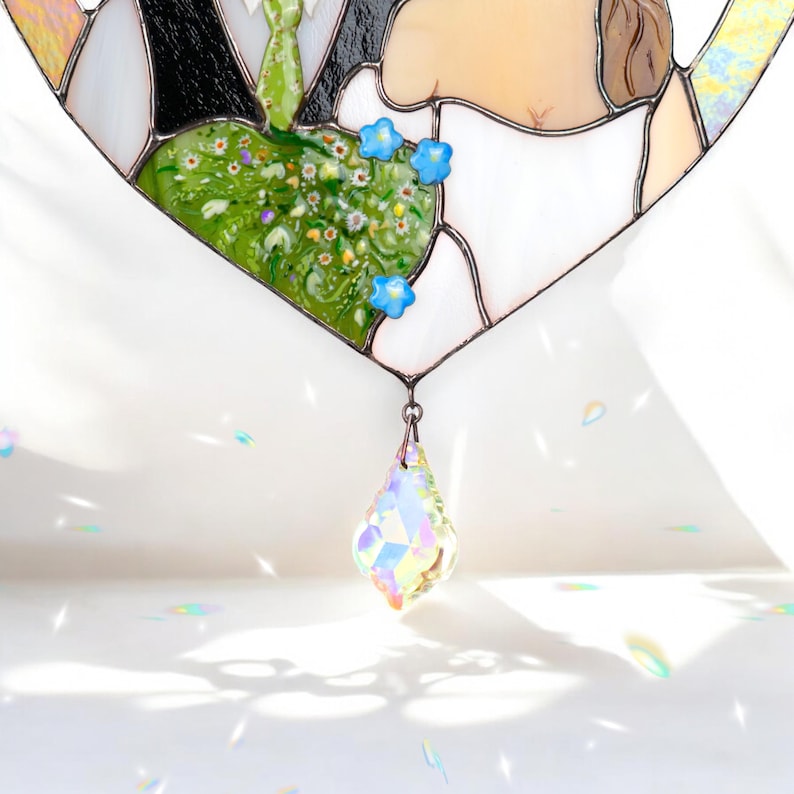 Close-up of stained glass wedding portrait showing the green floral heart detail and a hanging crystal prism catching light