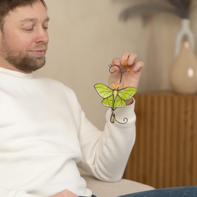 A man in a white sweatshirt holding the Luna Moth garden decoration. The photo demonstrates the size and scale of the piece, perfect for unique garden gifts.