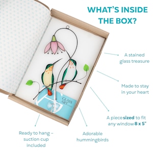 Unboxing view of a stained glass suncatcher featuring the hummingbirds and a pink flower in protective packaging