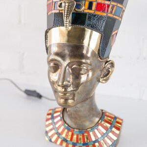 May include: Bronze bust of an Egyptian queen wearing a gold and blue mosaic crown and a colorful mosaic necklace.