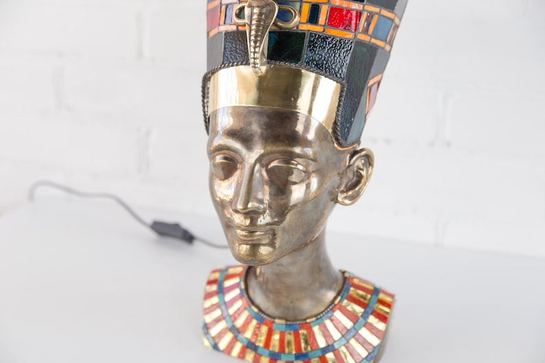 May include: Bronze bust of an Egyptian queen wearing a gold and blue mosaic crown and a colorful mosaic necklace.