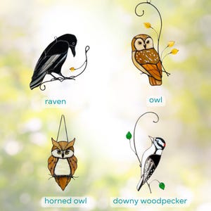 Stained glass bird suncatchers collection on decorative metal branches against a soft blurred background.