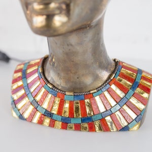 May include: Bronze bust of a woman wearing a colorful mosaic necklace with gold accents. The necklace is made of small, rectangular tiles in shades of red, blue, green, and gold.