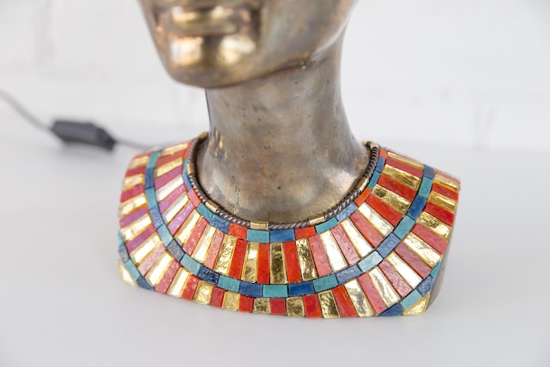 May include: Bronze bust of a woman wearing a colorful mosaic necklace with gold accents. The necklace is made of small, rectangular tiles in shades of red, blue, green, and gold.