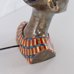 May include: Bronze bust of a woman with a gold and red mosaic collar. The bust is a table lamp with a black cord.