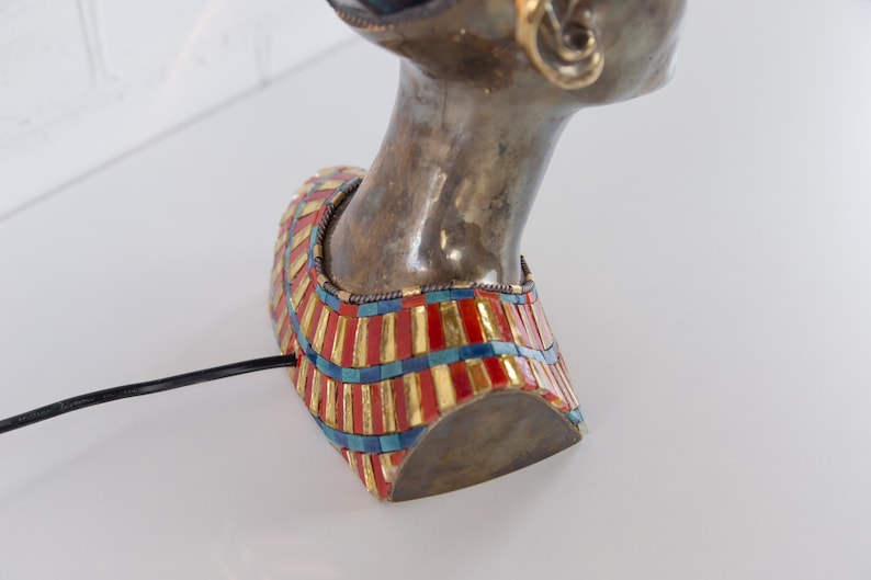 May include: Bronze bust of a woman with a gold and red mosaic collar. The bust is a table lamp with a black cord.