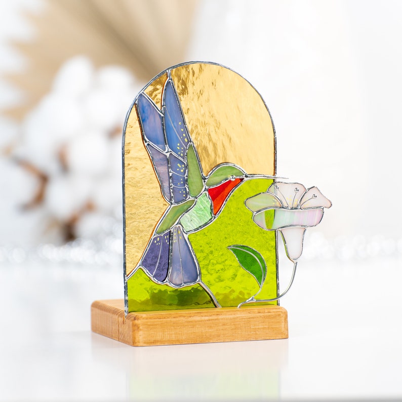 purple stained glass hummingbird with white flower on the wooden stand decorated by candle