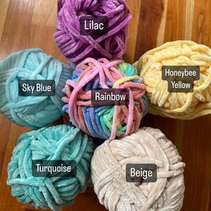 May include: Six balls of yarn in different colours: lilac, sky blue, rainbow, turquoise, beige, and honeybee yellow. The yarn is soft and fluffy, perfect for knitting or crocheting.