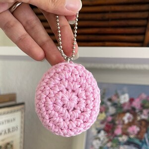 Puede incluir: Un llavero de c&iacute;rculo de crochet rosa con una cadena plateada.
