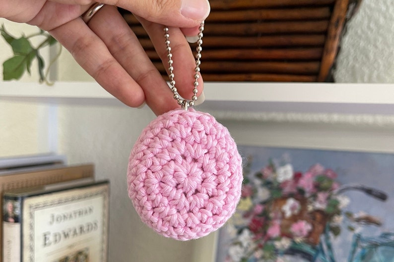 Puede incluir: Un llavero de c&iacute;rculo de crochet rosa con una cadena plateada.