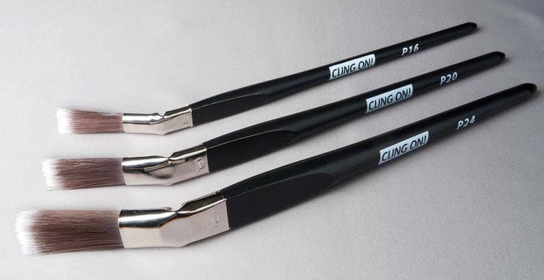 May include: Three angled paint brushes with black handles and silver ferrules. The brushes have brown and white bristles. The text "CLING ON!" is printed on the handles, along with the sizes P16, P20, and P24.