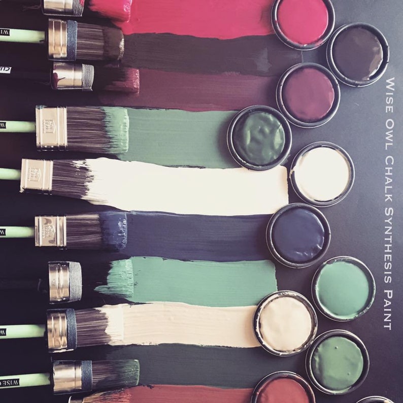May include: A set of paint pots with various colors of chalk paint, including red, burgundy, green, black, white, and cream. The paint pots are arranged in a row on a black surface.  The paint is labeled "WISE OWL CHALK SYNTHESIS PAINT".