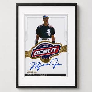 May include: A framed sports trading card featuring Michael Jordan in a black Chicago White Sox uniform. The card displays an MLB DEBUT patch, a blue ink autograph, and the text Michael Jordan MLB DEBUT 4.7.94 on a white background.