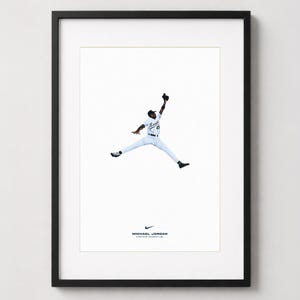 May include: A framed print featuring a baseball player in a white uniform with the number 45, captured in a mid-air jumping pose. Below the figure is a small Nike swoosh logo, the text MICHAEL JORDAN, and the text CAN FLY. DIFFERENT IS GOOD.