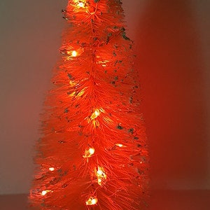 May include: A white artificial Christmas tree with red lights. The tree is decorated with white glitter and has a wooden base.