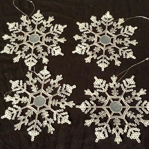 May include: Four white snowflake ornaments with a mirrored center. The snowflakes are made of plastic and have a beaded design.