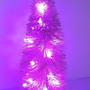 May include: A white artificial Christmas tree with purple lights. The tree is lit with white LED lights and has a wooden base.