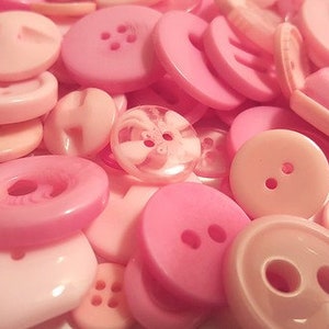 May include: A large assortment of pink plastic buttons of various sizes and styles. The buttons have two, three, or four holes.