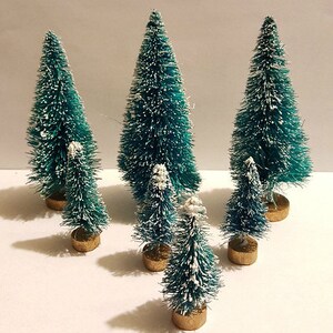 May include: Seven miniature artificial Christmas trees with a frosted white finish and green brush bristles. The trees are arranged in a row on a white surface.
