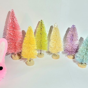 May include: A set of eight pastel-colored bottle brush trees. The trees are arranged in a rainbow order from pink to green. The trees are all the same size and shape.