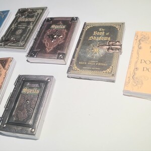 Könnte beinhalten: Eine Sammlung von acht kleinen, ledergebundenen Büchern mit Titeln wie "Spells", "The Book of Shadows" und "Potions & Poisons". Die Bücher haben eine Vintage-Ästhetik mit magischem Flair.
