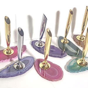 May include: Set of six agate pen holders with gold and silver pen rests. The agate slices are in various colors, including purple, pink, and green.