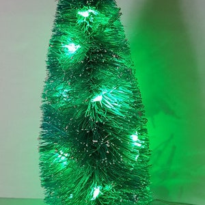 May include: A small green artificial Christmas tree with white flocking and green lights.