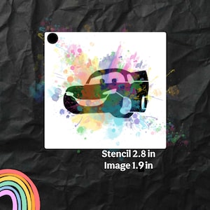 May include: A white square stencil featuring a cartoon car design with colorful watercolor paint splatters. The stencil measures 2.8 inches, and the image is 1.9 inches. The background is a dark, textured surface.