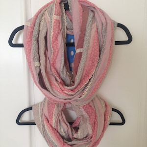 May include: A pink and gray striped infinity scarf with a crocheted trim. The scarf is folded in half and hung on a hanger.