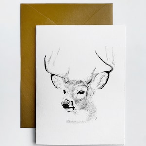 May include: A black and white illustration of a deer's head with antlers. The deer is looking to the left of the image. The illustration is on a white card with a gold envelope behind it.