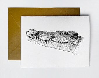 May include: A black and white pen and ink drawing of a crocodile's head. The drawing is on a white card with a gold envelope behind it. The artist's signature, "Ben Hayden", is in the bottom right corner.