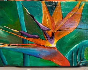 Puede incluir: Una pintura de una flor de ave del paraíso con colores naranja, azul, morado y verde sobre un fondo de madera.