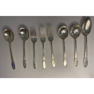 May include: A collection of antique silver-colored silverware, including spoons and forks. The spoons have rounded bowls and long handles. The forks have three tines. Each piece is engraved with the letter "S".