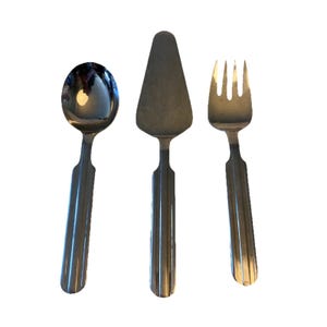 Puede incluir: Juego de tres utensilios de servir de acero inoxidable: una cuchara, una espátula para pastel y un tenedor. Cada pieza tiene un mango acanalado y una superficie pulida y reflectante. La cuchara tiene un cuenco redondeado, la espátula es triangular y el tenedor tiene tres púas.