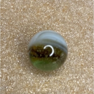 May include: A green, brown and white marble with a swirl pattern. The marble has a clear, glassy finish.