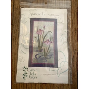 May include: A quilting pattern for a wall hanging featuring Japanese Irises in shades of pink and purple. The pattern is titled "Japanese Iris" and is a design by Janet Pittman. The pattern is 16 x 28 inches.
