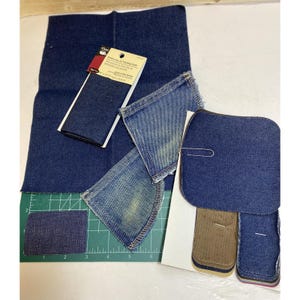 May include: Assortment of blue denim fabric scraps in various sizes and shapes, including a square, rectangle, and two triangles. The fabric is a dark blue color and has a woven texture. There is a small white label with the text "Denim Jean or Padding Cloth" on it.