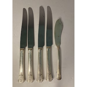 May include: Set of five silver-plated knives with ornate handles. The knives include four dinner knives and one butter knife.