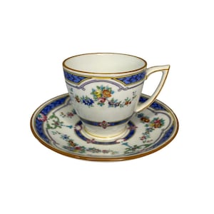 Pode incluir: Um conjunto de chávena e pires de porcelana branca com um padrão floral em tons de azul, amarelo, rosa e verde. A chávena e o pires têm uma borda dourada.