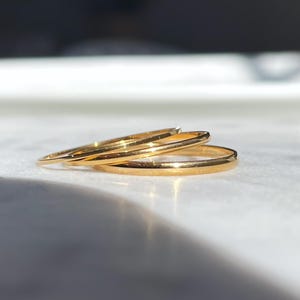 May include: Three gold stacking rings, each with a smooth, polished finish. The rings are stacked on top of each other, with the largest ring on the bottom and the smallest ring on top.