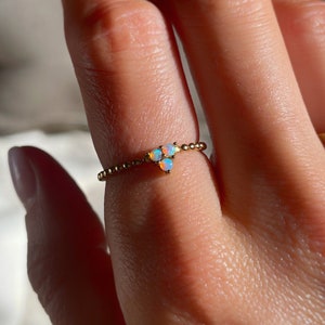 May include: A gold ring with three small opal stones set in a delicate, beaded band.