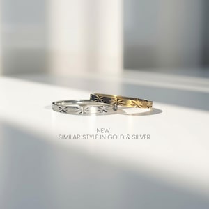 Peut inclure: Deux bagues fines en m&eacute;tal, une argent&eacute;e et une dor&eacute;e, pr&eacute;sentant chacune un motif d'&eacute;toile grav&eacute; sur l'anneau. Le texte en dessous indique : NEW! SIMILAR STYLE IN GOLD & SILVER.