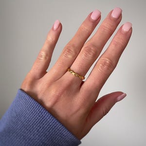 Peut inclure: Une fine bague en or pr&eacute;sentant un motif r&eacute;p&eacute;titif de petites &eacute;toiles ou de rayons de soleil grav&eacute;s sur toute la surface ext&eacute;rieure. Le m&eacute;tal a une finition polie et le design se compose d'&eacute;toiles alternant avec de petites indentations circulaires.