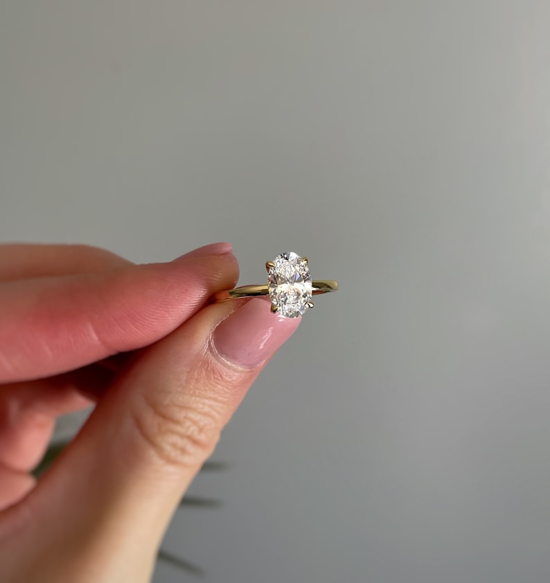 A  solitaire ring featuring an oval shaped cubic zirconia with a gold band and four prong setting