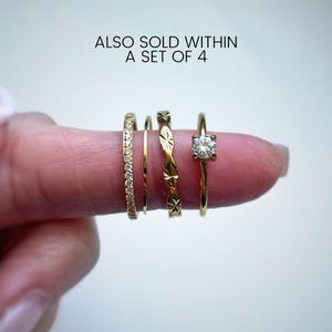 Peut inclure: Un ensemble de quatre bagues dor&eacute;es comprenant un anneau avec de petites pierres claires, un anneau fin uni, un anneau &agrave; motif &eacute;toil&eacute; r&eacute;p&eacute;titif et une bague solitaire avec une pierre claire. Le texte indique : ALSO SOLD WITHIN A SET OF 4.