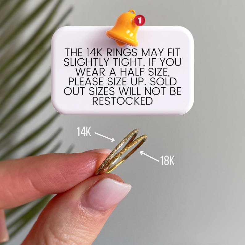 May include: Two thin gold rings, one labeled 14K with a textured surface and one labeled 18K with a smooth surface. A white rectangular sign above reads: THE 14K RINGS MAY FIT SLIGHTLY TIGHT. IF YOU WEAR A HALF SIZE, PLEASE SIZE UP. SOLD OUT SIZES WILL NOT BE RESTOCKED.