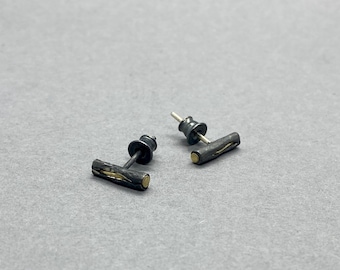 May include: A pair of black and gold stud earrings. The earrings are made of a textured metal and have a thin gold band around the centre.