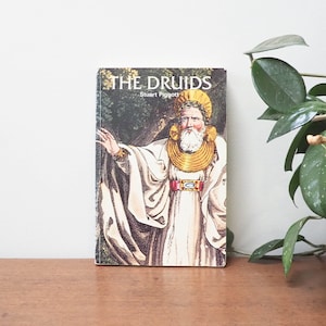 May include: A book titled "The Druids" by Stuart Piggott, featuring a colourful illustration of a man with a beard and a golden necklace on the cover.